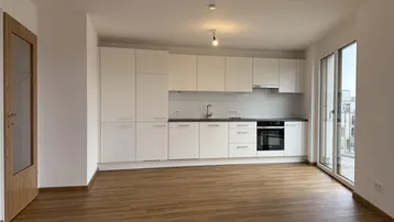 Moderne, helle Küche mit weißen Schränken, integrierten Geräten und Zugang zu einem Balkon.