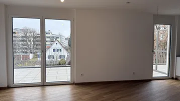 Heller Wohnbereich mit großen Fenstertüren und Zugang zu einer Terrasse oder einem Balkon.