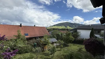 Blick auf das Haus mit rotem Ziegeldach, üppigem Garten und malerischer Bergkulisse im Hintergrund.