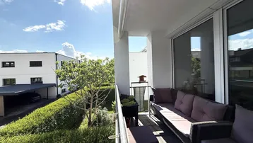 Sonniger Balkon mit bequemen Loungemöbeln und Blick auf die umliegende Wohnanlage.