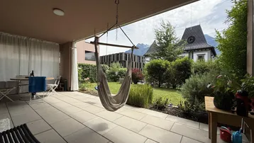 Geräumige Terrasse mit Hängematte und Sitzbereich, umgeben von Grünflächen und Blick auf die Umgebung.