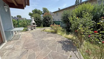 Große gepflasterte Terrasse mit festem Grillbereich und Blick ins Grüne.