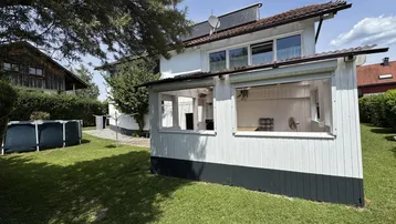 Rückseite des Hauses mit Wintergarten, Rasenfläche und einem Aufstellpool im Garten.