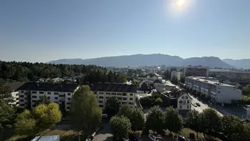 Weitläufige Stadtansicht mit Bergen im Hintergrund unter strahlend blauem Himmel.