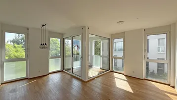 Helles Wohnzimmer mit Holzboden, großen Fenstern und Zugang zu einem Balkon.