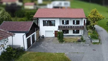 Traditionelles Einfamilienhaus mit Satteldach, Balkon und angrenzendem Nebengebäude in ländlicher Umgebung.