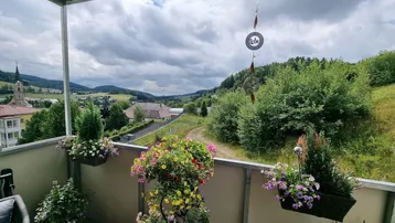 Balkon mit bunten Blumen und weitem Blick über die hügelige Landschaft und das Dorf.