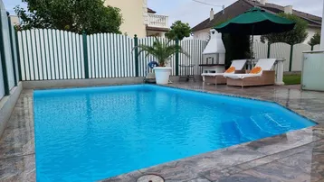 Außenbereich mit großem Pool, Liegestühlen, Sonnenschirm und Grillplatz für entspannte Stunden.