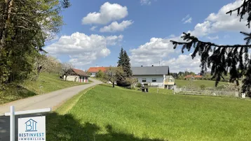Ländliches Anwesen umgeben von grünen Wiesen und Bäumen unter blauem Himmel.