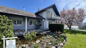 Ansicht des Hauses mit gepflegtem Garten, Teich und blühendem Baum im Frühling.