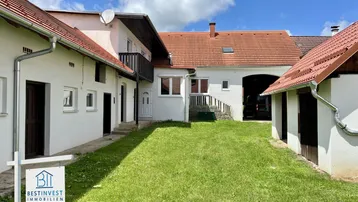 Blick auf den Innenhof der Immobilie mit mehreren Gebäuden und grünem Rasen unter blauem Himmel.