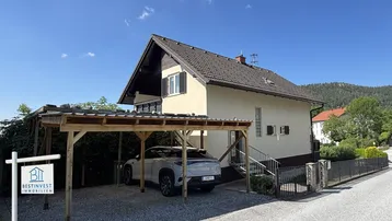 Einfamilienhaus mit Carport und gepflegter Zufahrt unter blauem Himmel.
