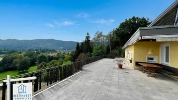 Große geflieste Terrasse mit Holzzaun und weitem Blick über die Landschaft und Berge.