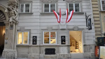 Historische Fassade eines gut erhaltenen Gebäudes mit dekorativen Elementen, Fenstern und einem Ladeneingang auf Straßenniveau.