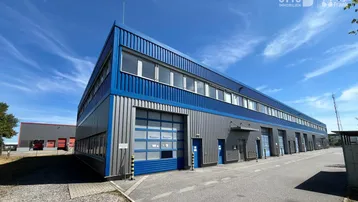 Modernes Industriegebäude mit blauer und grauer Fassade, mehreren Rolltoren und großen Fenstern unter blauem Himmel.