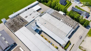 Luftaufnahme eines großen Industrie- und Gewerbekomplexes mit mehreren Hallen und umliegenden Grünflächen.