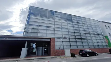 Modernes Geschäftsgebäude mit großer Glasfassade und Ziegelmauerwerk, inklusive Einfahrt zur Tiefgarage.