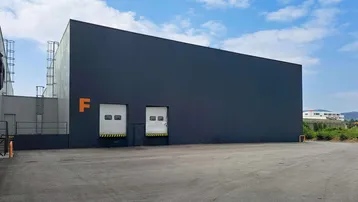 Moderne Industriefassade in Dunkelgrau mit orangefarbenen Akzenten und zwei Rolltoren unter blauem Himmel.