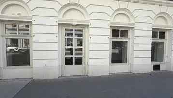 Die weiße Fassade des Erdgeschosses zeigt eine Eingangstür und mehrere Fenster zur Straße hin.