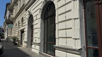 Historische Fassade eines eleganten Gebäudes mit großen Bogenfenstern und dekorativen Elementen an einem sonnigen Tag.