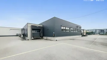 Modernes Gewerbegebäude mit dunkler Fassade, großen Fenstern und Laderampe auf einem weitläufigen Parkplatz.
