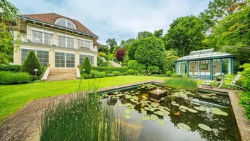 Großer gepflegter Garten mit Zierteich, weitläufiger Rasenfläche und einem eleganten Wintergarten.