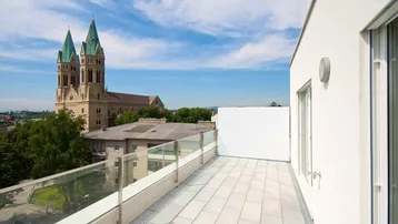 Große Dachterrasse mit Glasgeländer und weitem Blick auf die Stadt und eine Kirche.