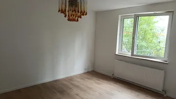 Heller Raum mit Laminatboden, großem Fenster und einer dekorativen Deckenleuchte.