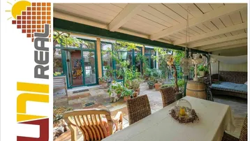 Gemütliche überdachte Terrasse mit Esstisch, Rattanmöbeln und üppiger Bepflanzung, ideal für entspannte Stunden im Freien.