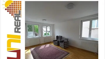 Helles Wohnzimmer mit Holzfußboden, Teppich und zwei Sesseln, umgeben von mehreren Fenstern.