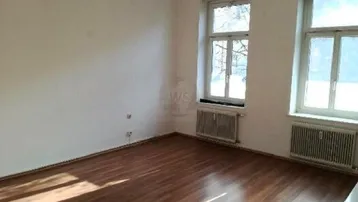 Helles Zimmer mit zwei Fenstern, Heizkörpern und Holzdielenboden, ideal als Wohn- oder Schlafzimmer.