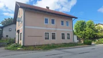 Fassade eines Wohnhauses mit mehreren Fenstern und einem Satteldach unter blauem Himmel.