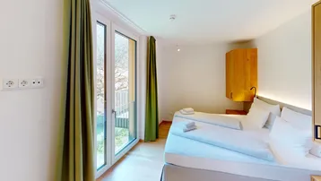 Schlafzimmer mit Holzboden, weißem Bett und französischem Balkon, der viel Licht spendet.
