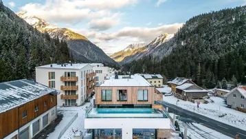 Moderne Wohnanlage in alpiner Winterlandschaft mit Infinity-Pool auf dem Dach und Bergblick.