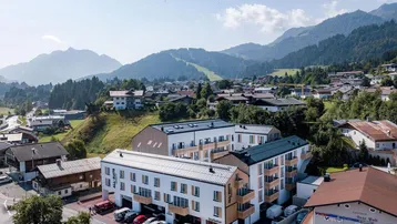 Luftaufnahme eines modernen Apartmentkomplexes in einer malerischen Berglandschaft mit umliegenden Häusern.