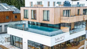 Modernes Gebäude mit Holzfassade und einem beeindruckenden Infinity-Pool auf der Dachterrasse, umgeben von verschneiten Bäumen.