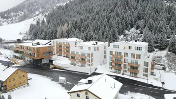 Moderne Wohngebäude in einer verschneiten Berglandschaft, umgeben von dichtem Wald.