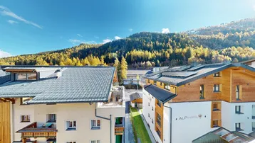 Moderne Gebäude mit Holzfassaden und Ziegeldächern in einer bergigen, bewaldeten Landschaft.
