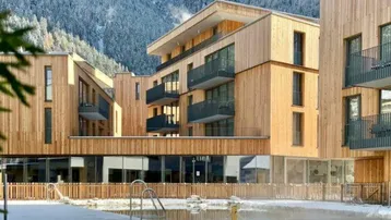 Moderne Gebäude mit Holzfassaden und einem Außenpool vor einer beeindruckenden Bergkulisse im Schnee.