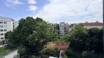 Blick von oben auf einen grünen Innenhof mit Bäumen, Spielplatz und umliegenden Gebäuden unter blauem Himmel.