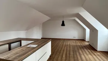 Geräumiger offener Wohnbereich im Dachgeschoss mit Holzboden und moderner Küchenzeile.