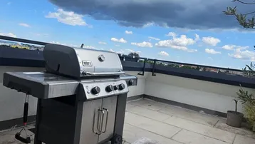 Geräumige Dachterrasse mit Gasgrill und weitem Blick unter bewölktem Himmel.
