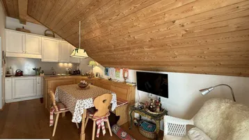 Offener Wohn-Essbereich mit integrierter Küche, Holzboden und schräger Holzdecke.