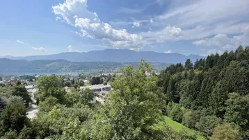 Panoramablick auf die umliegende Berglandschaft, einen See und grüne Wälder unter blauem Himmel.