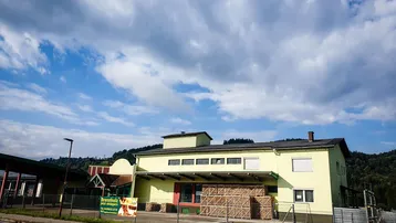 Gelbes Geschäftsgebäude mit Vordach und Holzstapeln unter einem bewölkten Himmel.