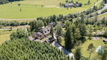 Weitläufige Luftaufnahme des Anwesens in einer malerischen Landschaft mit Wäldern, Feldern und einem Fluss.