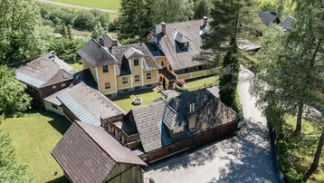 Luftaufnahme des weitläufigen Anwesens mit mehreren Gebäuden, umgeben von grünen Bäumen und Wiesen.