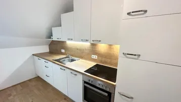 Moderne Einbauküche mit weißen Hochglanzschränken, Holzoptik-Arbeitsplatte und Dachschräge.