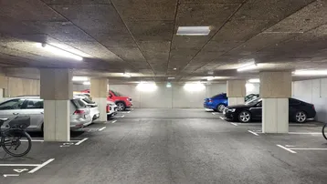 Geräumige Tiefgarage mit markierten Stellplätzen und abgestellten Fahrzeugen sowie Fahrrädern.