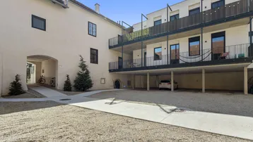 Innenhof eines Gebäudekomplexes mit Kiesfläche, Durchgang und Balkonen an einem modernen Anbau.
